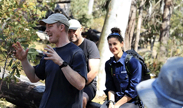 Jack Riewoldt speaking to a group of people in native bushland. He wears a navy top and grey cap. There are people in the background listening intently.