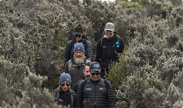 Jack Riewoldt walks among a group of bushwalkers along the Three Capes in Tasmania. They are surrounded by thick bushland and wearing dark jackets and beanies.