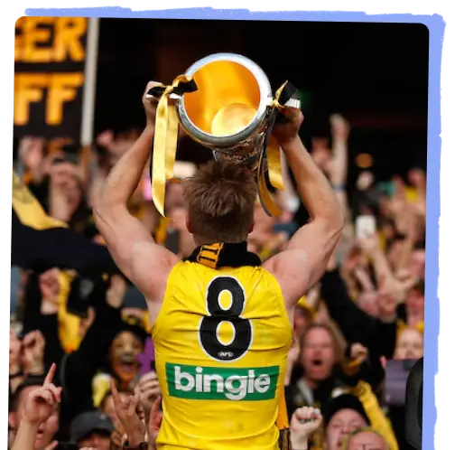 Jack Riewoldt holding the AFL premiership cup. He wears his yellow guernsey number eight, and is facing a celebratory crowd. Image Credit: AFL Media, Michael Wilson.